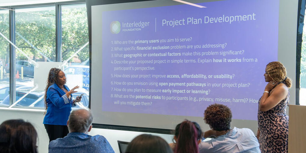 Two presenters speaking in front of a slide titled “Project Plan Development,” sharing ideas and strategies